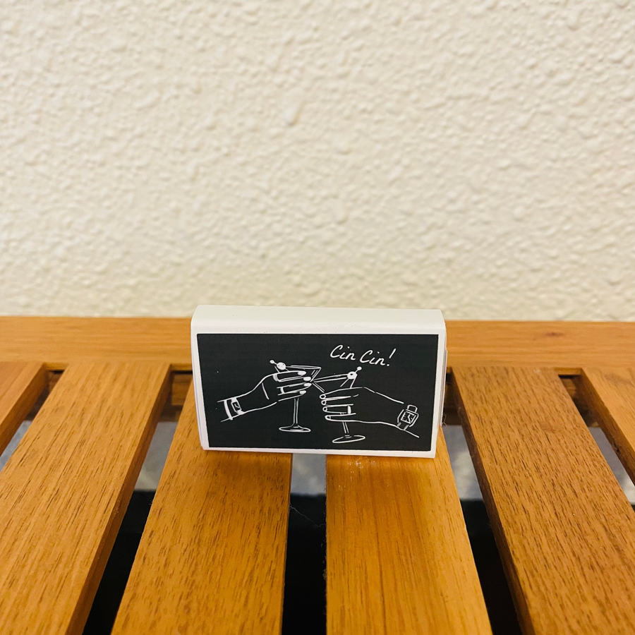 Small black and white card with a design of two hands clinking glasses on a wooden surface.